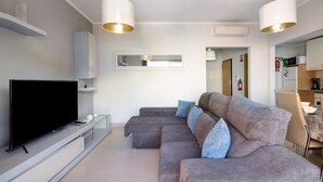 A modern living room with a flat-screen TV, a sectional sofa, and pendant lighting.