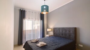 A hotel room with a bed, a bedside lamp, a window with curtains, and a hanging light fixture.