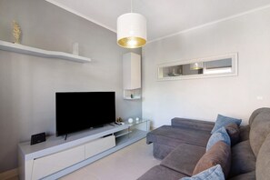A modern living room with a flat-screen TV, a glass coffee table, a sofa, and a pendant light. - Royal Cabanas Golf 85 Apartment with Shared Pool, Garden, and Air Conditioning (Cabanas de Tavira)