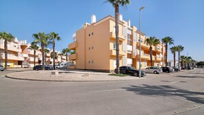 A multi-story residential building with balconies, parked cars, and palm trees. - Apartment 'Royal Cabanas Golf 88' with Shared Pool, Shared Garden and Air Conditioning (Cabanas de Tavira)
