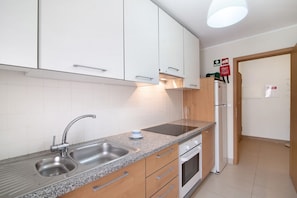 A kitchen with white cabinets, a granite countertop, a stainless steel sink, a built-in oven, and a refrigerator.