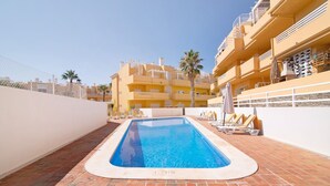Une piscine au sol en briques, entourée de chaises longues et de parasols, avec un bâtiment en arrière-plan.