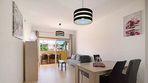 Un salon moderne avec un coin repas, comprenant un canapé, une table basse et une table à manger avec des chaises. Deux lampes suspendues sont placées au-dessus de la table à manger.