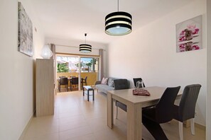 Un salon moderne avec un coin repas, comprenant un canapé, une table basse et une table à manger avec des chaises. Deux lampes suspendues sont placées au-dessus de la table à manger.