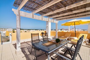 A terrace with a glass table, chairs, and a yellow umbrella.
