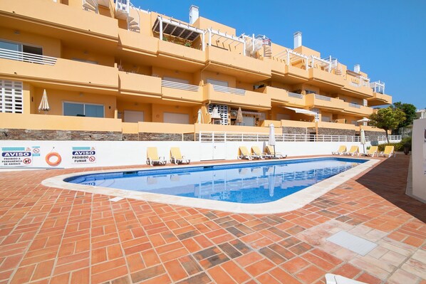 A multi-story building with a swimming pool, outdoor seating, and balconies.