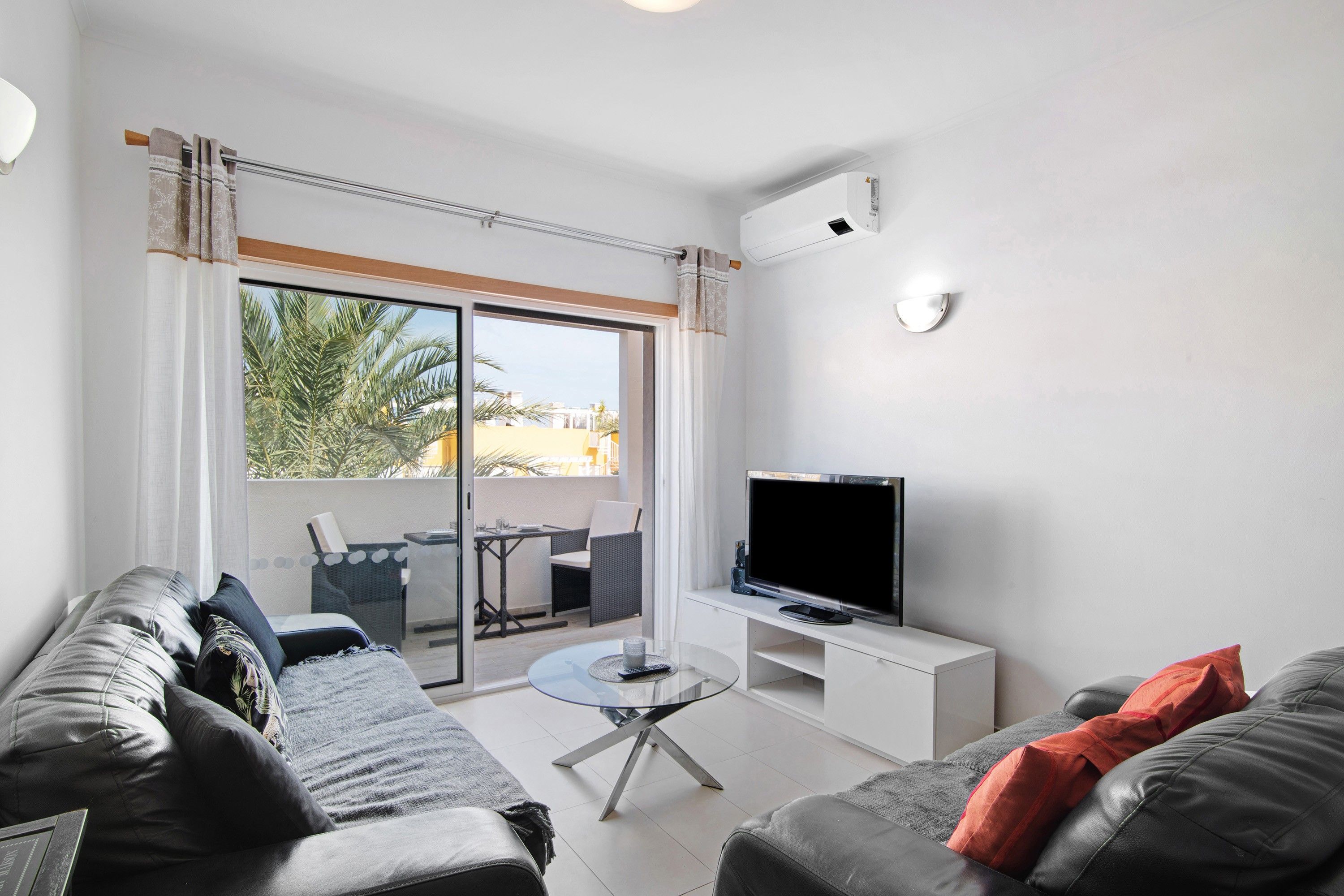 Ein modernes Wohnzimmer mit einer Couch, einem Couchtisch, einem Flachbildfernseher und einem Balkon mit Gartenmöbeln.