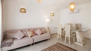 A living room with a sofa, a glass dining table with chairs, and two wall-mounted lamps. - Holiday Apartment "Urbanização Lagar 133" with Sea View & Private Balcony (Conceição de Tavira)