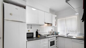 A modern kitchen with white cabinets, a stove, microwave, and a sink. - Holiday Apartment "Urbanização Lagar 133" with Sea View & Private Balcony (Conceição de Tavira)