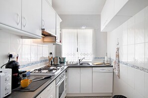 Une cuisine de taille réduite, avec des meubles blancs, une cuisinière à gaz, une machine à café et un évier.