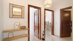 A hallway with wooden doors, a wall-mounted mirror, and a floor lamp. - Holiday Apartment "Urbanização Lagar 133" with Sea View & Private Balcony (Conceição de Tavira)