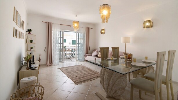 A modern living room with a glass dining table, wicker chairs, a sofa, and a glass coffee table. There are two pendant lights, a wall-mounted lamp, and a view of the outside through a glass door. - Holiday Apartment "Urbanização Lagar 133" with Sea View & Private Balcony (Conceição de Tavira)
