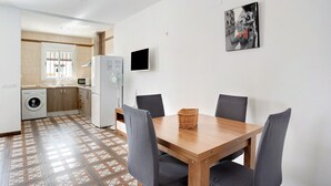 A dining area with a wooden table and chairs, a washing machine, a microwave, and a television in the background. - Holiday Home 'Casa Cala Del Aceite 1' with Private Pool, Private Terrace and Wi-Fi (Conil de la Frontera)