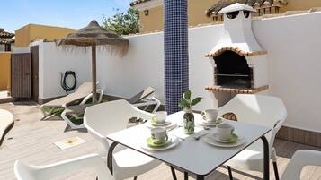 An outdoor patio with a table set for two, a grill, and a water fountain.