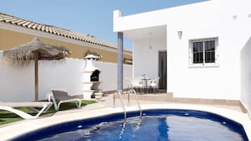 A swimming pool with lounge chairs, a barbecue area, and a patio with a table and chairs.
