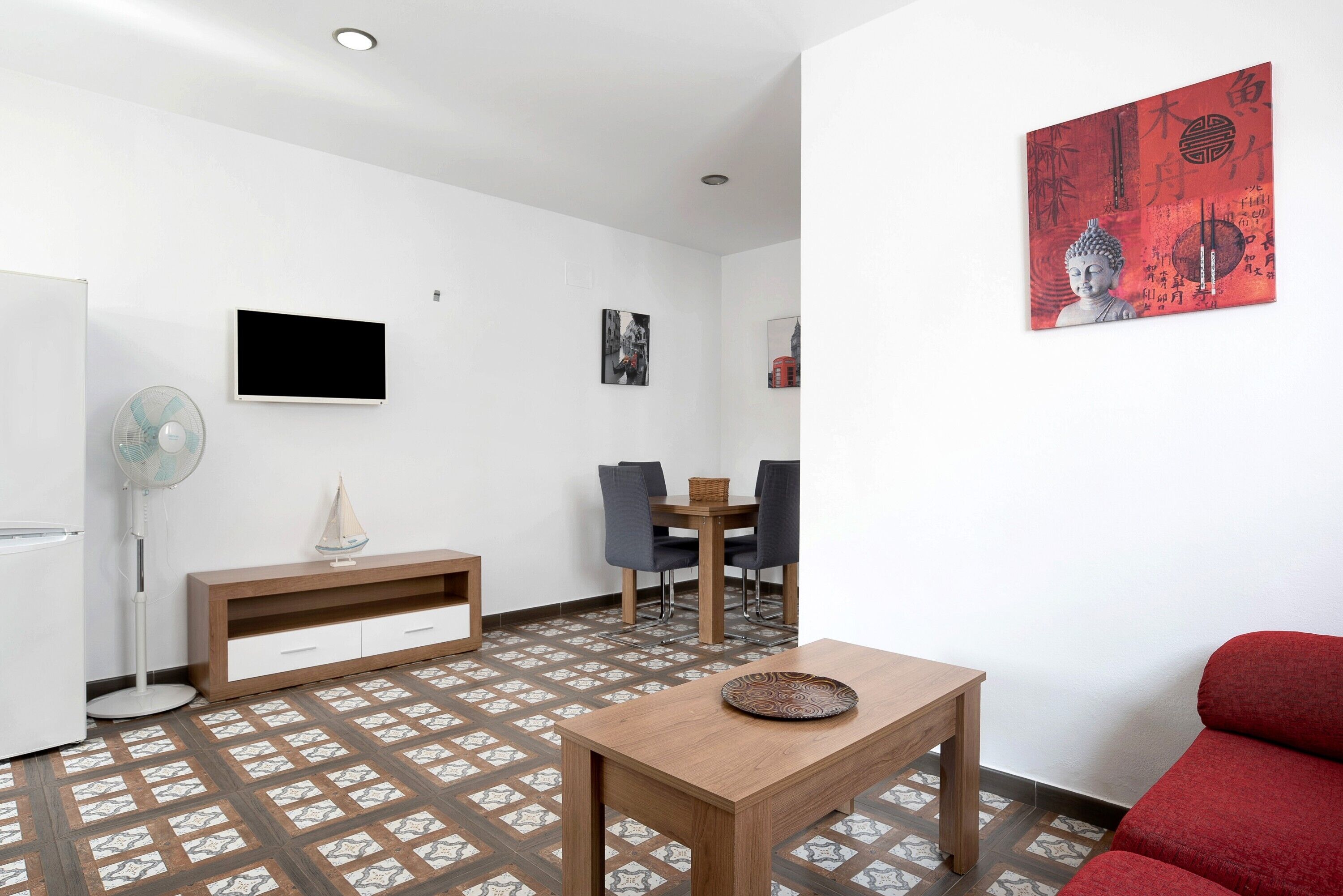 A modern living room with a wooden table, a red sofa, a TV, a fan, and a dining area with chairs and a table.