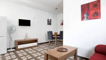 A modern living room with a wooden table, a red sofa, a TV, a fan, and a dining area with chairs and a table.