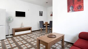 Una sala moderna con una mesa de madera, un sofá rojo, un televisor, un ventilador y un comedor con sillas y una mesa.