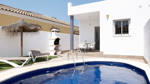 Una piscina con sillas de descanso, un área de barbacoa y un patio con mesa y sillas.