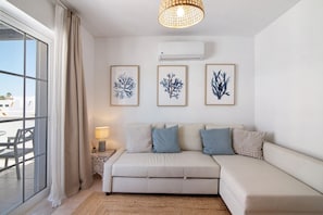 Un salon moderne avec un canapé, une table d’appoint surmontée d’une lampe, et des œuvres d’art encadrées accrochées au mur.