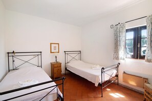 Ein Zimmer mit zwei Betten, einem Holznachttisch, einem Heizkörper und einem Fenster mit Vorhängen.
