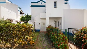 A white building with blue trim, a stone pathway, and green and red flowering plants.