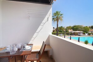 Ein Balkon mit Esstisch, im Hintergrund ein Pool und eine Palmenbaum.