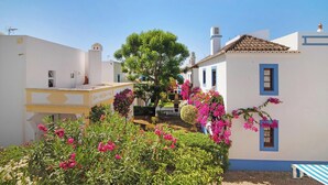 A courtyard with white buildings, a tree, and pink flowers.