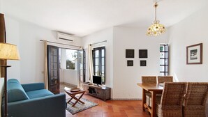 A living room with a sofa, dining table, chairs, a TV, and a hanging light fixture.