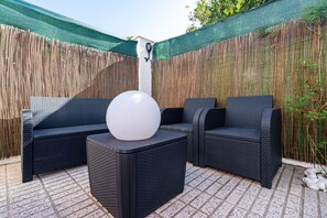 A patio with wicker furniture, a round table, and a green mesh screen. - Villa "Traditional" with Private Pool & Wi-Fi (Creixell)