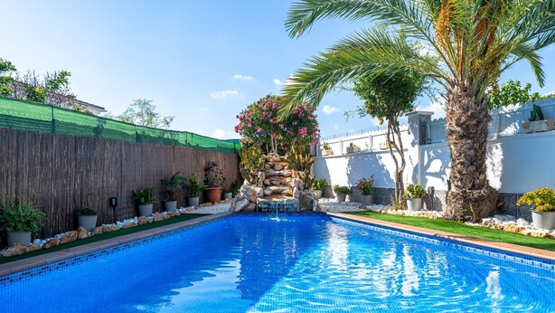 A swimming pool with a stone waterfall feature, surrounded by potted plants and palm trees. - Villa "Traditional" with Private Pool & Wi-Fi (Creixell)
