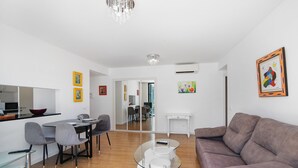 En moderne stue med et sofabord i glas, en sofa og et spiseområde med stole og bord.