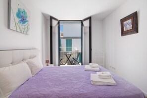 A bedroom with a bed, a window, a balcony, and a painting on the wall.