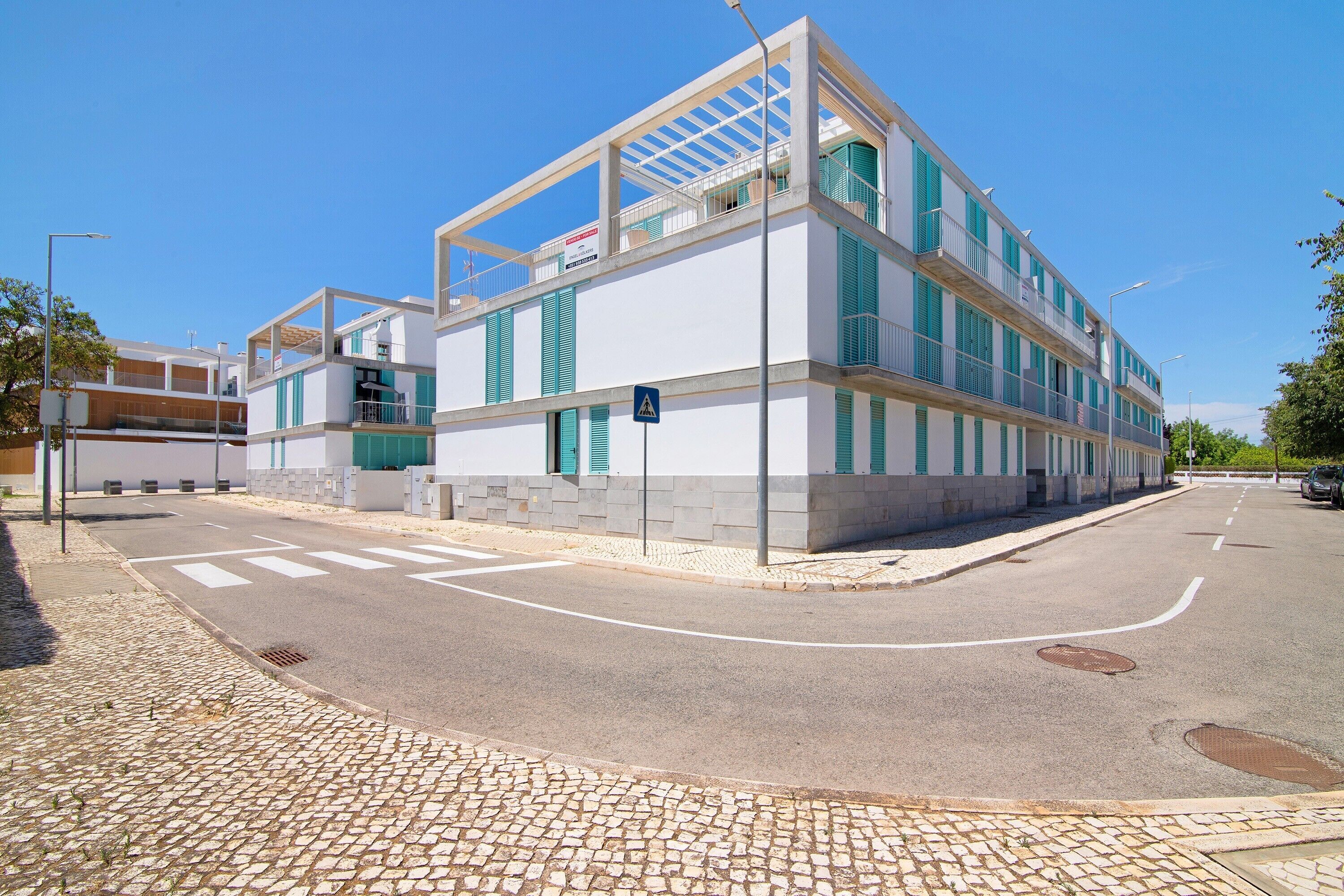 Un bâtiment moderne à la façade blanche, aux volets verts et doté d’un passage piéton.