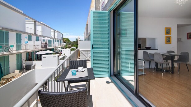 En balkon med udesiddeplads, et spiseområde med stole og bord, samt udsigt til den tilstødende bygning.