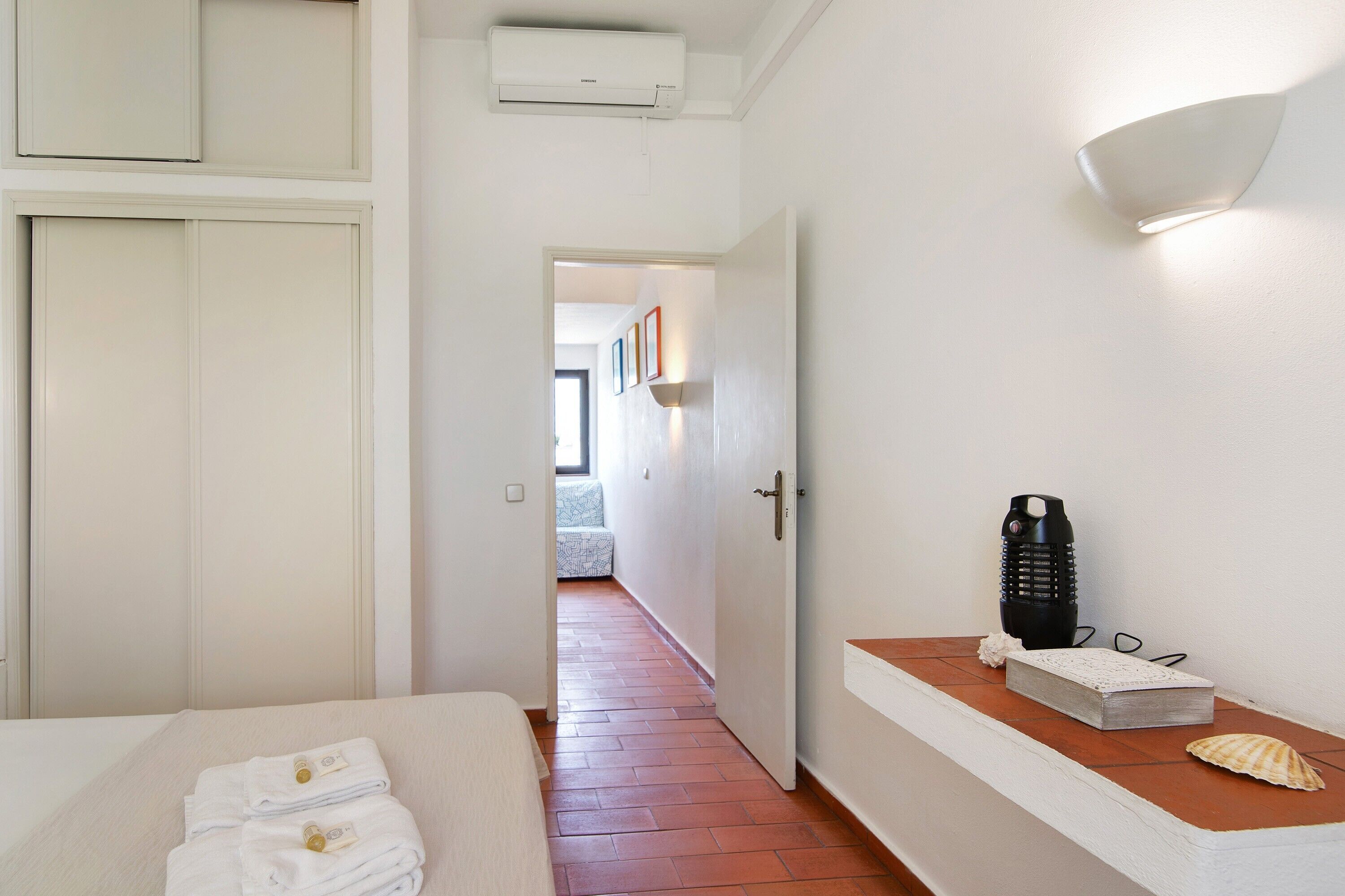 Hotelkamer met een bed, nachtkastje met een lamp, een wandlamp en een deur naar een andere kamer.