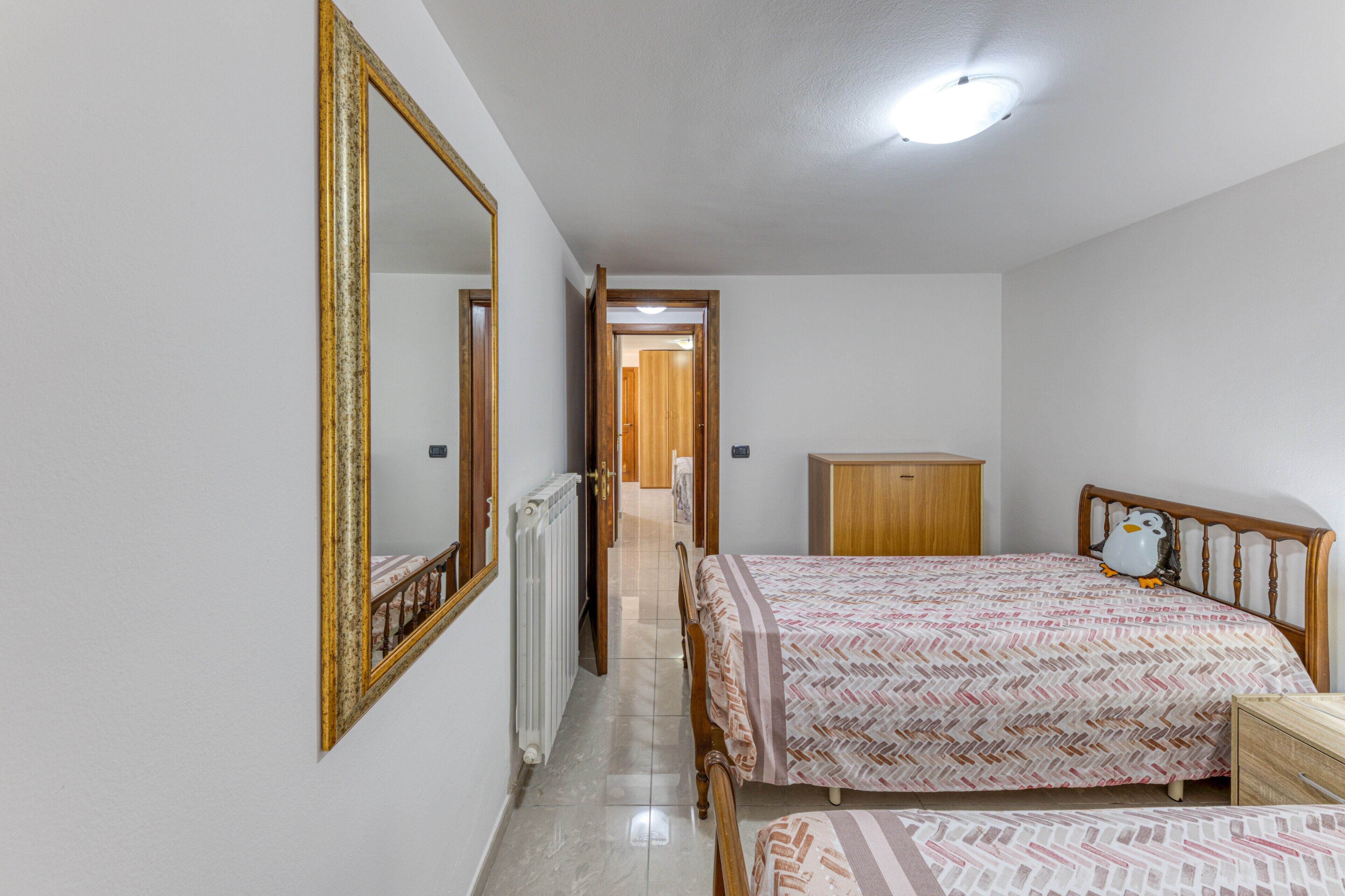 Un dormitorio con cama, cómoda, espejo y radiador.