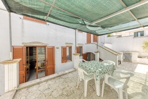 Une terrasse extérieure couverte, avec une table et des chaises, des volets en bois et un escalier.