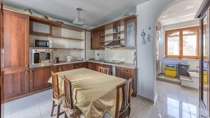 A kitchen with wooden cabinets, a microwave, an oven, and a dining table with chairs. - Apartment "Casa di Marika" with Private Terrace and Air Conditioning (marina di leuca)
