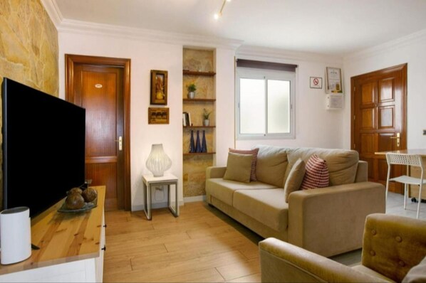 A living room with a sofa, a TV, a small table, and a window.