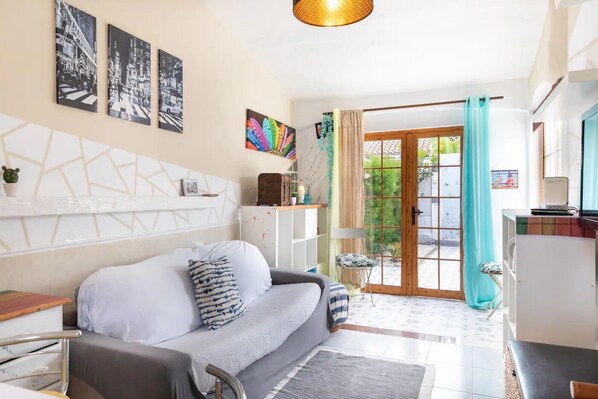 Uma sala de estar moderna com um sofá, área de jantar, cozinha e vista através de uma porta de vidro.
