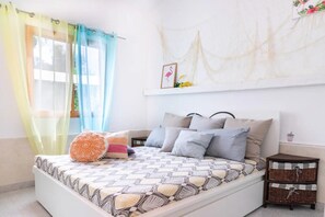Um quarto com cama, cortinas, uma obra de arte na parede e uma pequena mesa de cabeceira.