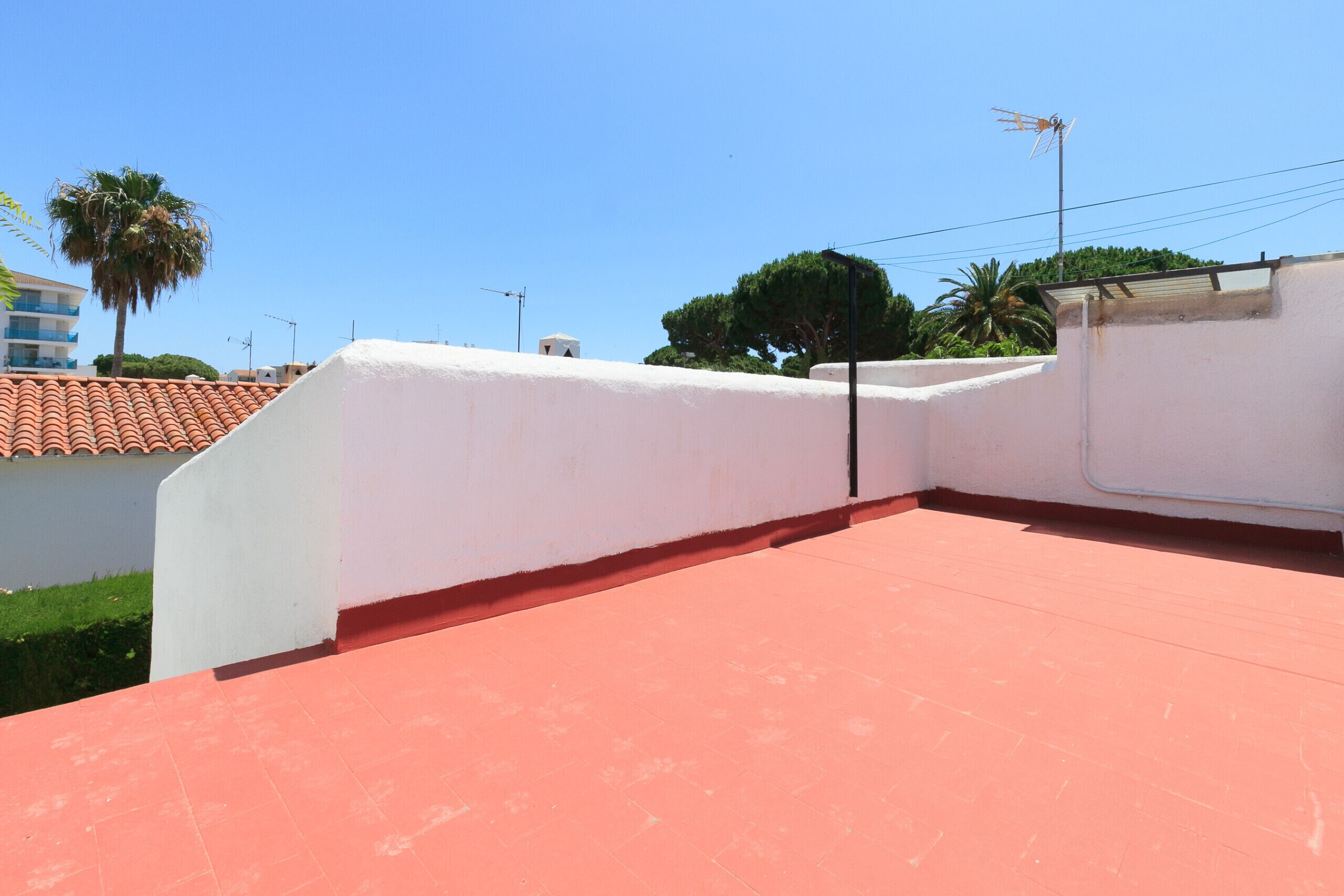 A rooftop terrace with a red floor, white walls, and a clear blue sky.