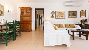A living room with a sofa, chairs, a wooden cabinet, and wall-mounted artwork.