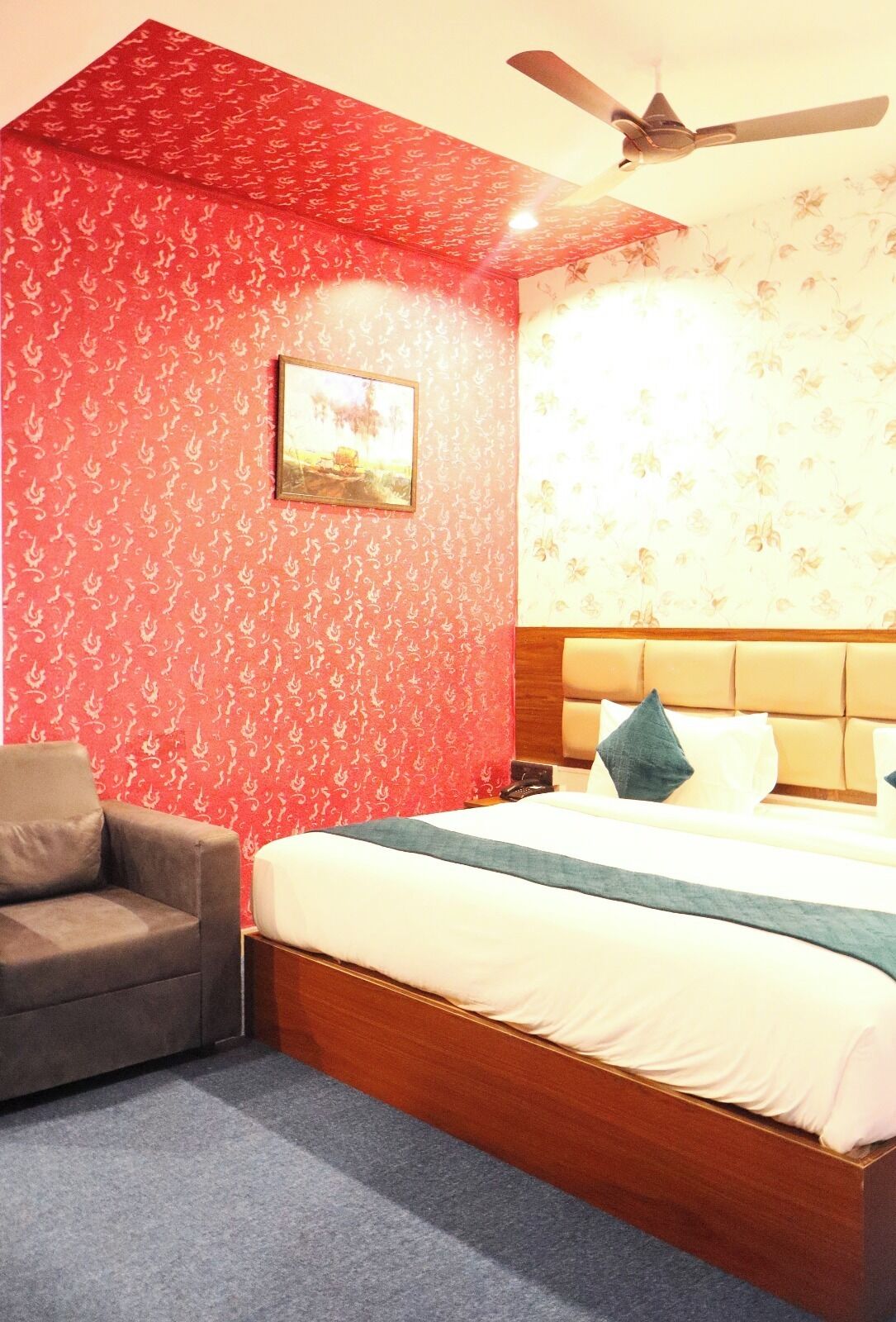 A hotel room with a bed, a chair, a ceiling fan, and a painting on the wall.