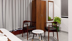 A hotel room with a bed, two wooden chairs, a small table, a wardrobe, a mirror, and a potted plant. - The Elite Hotel  (Hyderabad)
