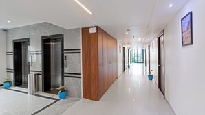A modern hallway with elevators, a wooden panel, and potted plants. - The Elite Hotel  (Hyderabad)