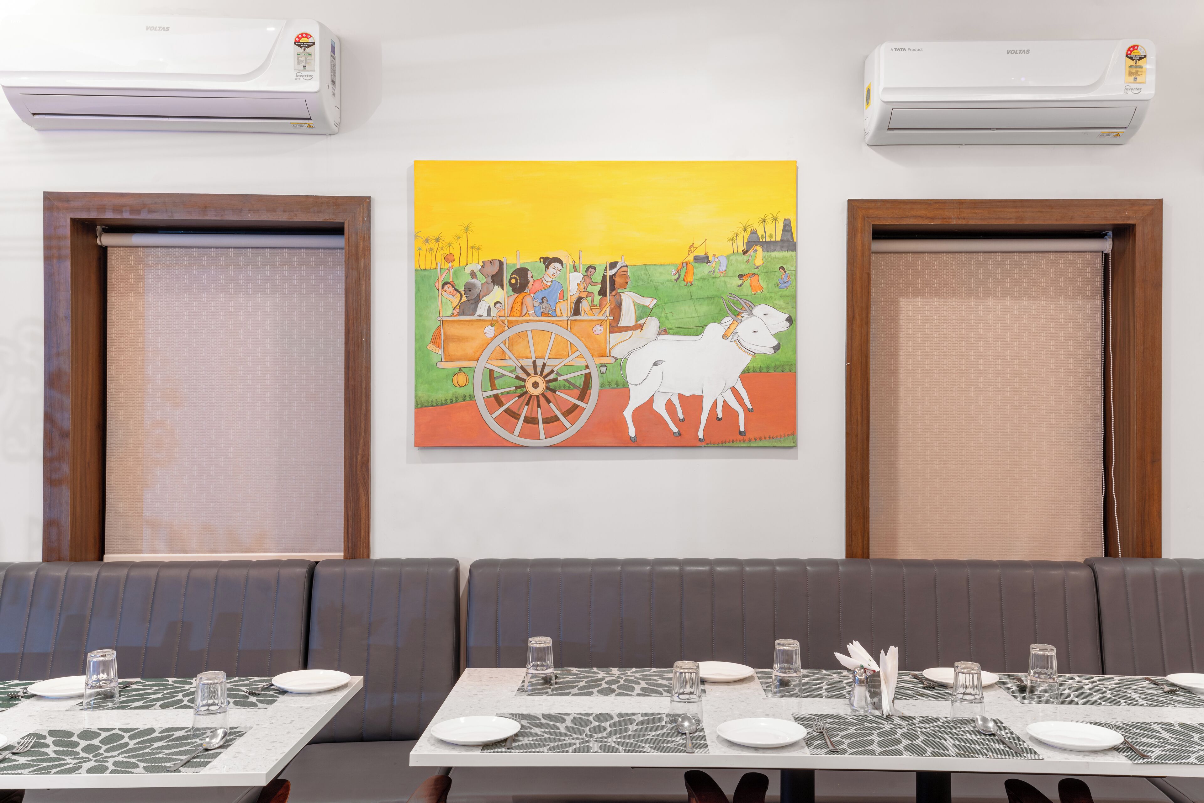 Un restaurante con zona de comedor que incluye mesas para dos, unidades de aire acondicionado y un cuadro colgado en la pared.