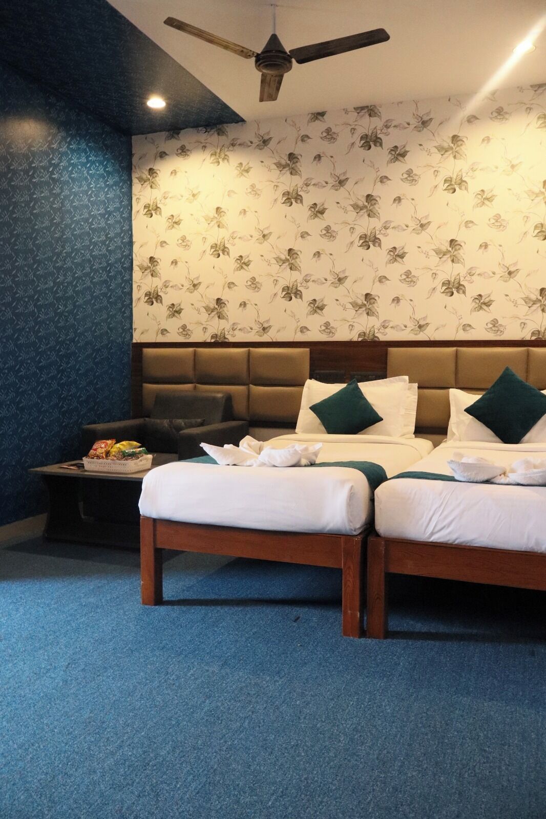 A hotel room with a large bed, a small sofa, a ceiling fan, and a wall with floral wallpaper.