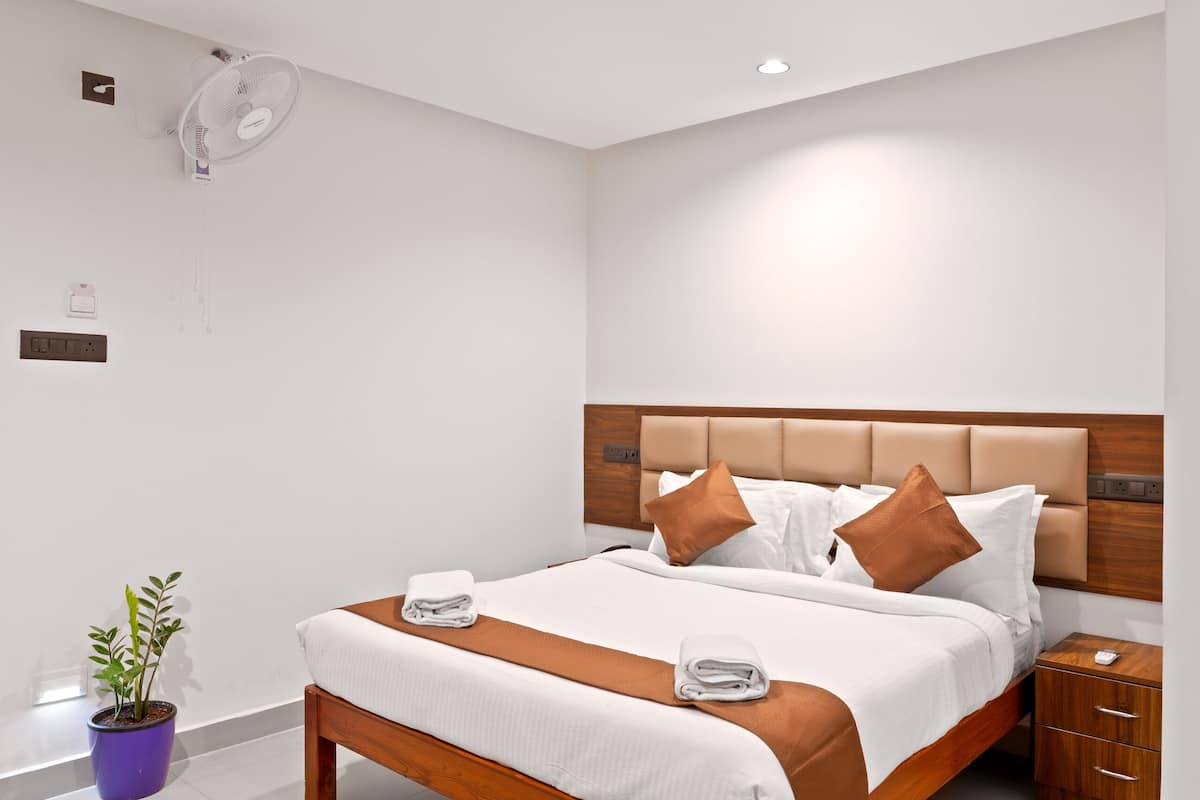 A modern hotel room with a large bed, wooden headboard, white bedding, and a small bedside table with a lamp.